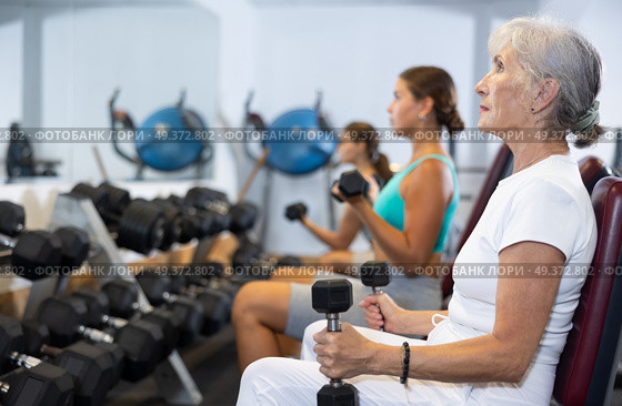 Mature sportswoman doing exercises with a barbell and dumbbells in gym. Стоковое фото, фотограф Яков Филимонов / Фотобанк Лори
