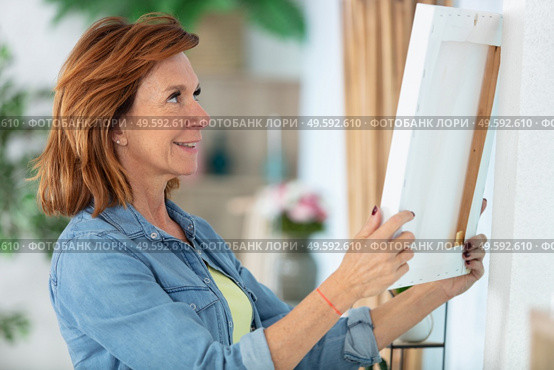 mature woman hanging picture on wall. Стоковое фото, агентство Ingram Publishing / Фотобанк Лори