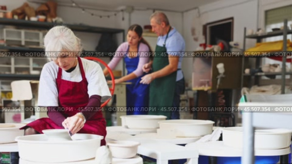 Mature woman learning how to create pottery on potter wheel in a workshop. Стоковое видео, видеограф Яков Филимонов / Фотобанк Лори