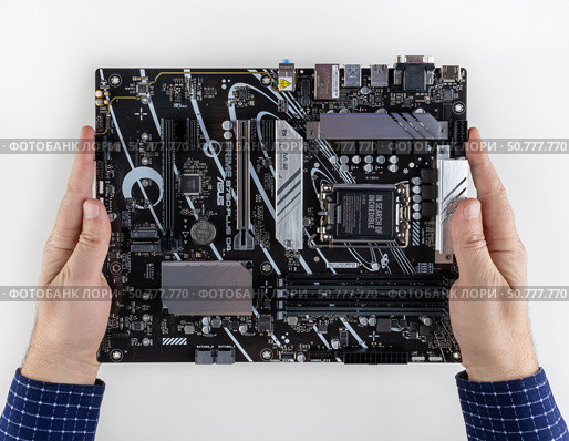 Maykop, Russia - February 18, 2025: A man holds in the hands of a new asus prime b - 760 plus d4 motherboard on a light gray background top view. Редакционное фото, фотограф Андрей С / Фотобанк Лори