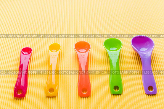 Мерные ложки на желтом фоне. Разноцветные пластиковые мерные ложки. Measuring spoons on a yellow background. Multi-colored plastic measuring spoons. Стоковое фото, фотограф Ольга Митряева / Фотобанк Лори