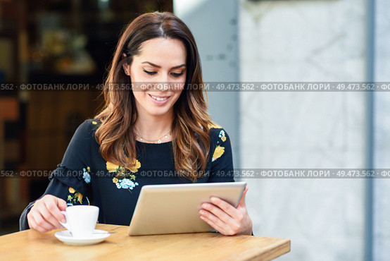 Middle-aged woman using tablet on coffee break in urban cafe bar. Young female sitting at table at cafe. Girl with california highlights hairstyle.. Middle-aged woman using tablet on coffee break in urban cafe bar. Стоковое фото, агентство Ingram Publishing / Фотобанк Лори