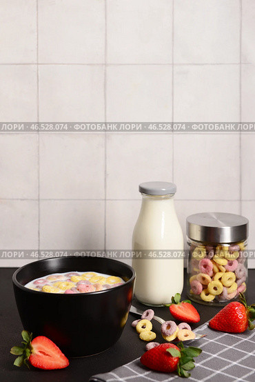 Миска с цветными сладкими колечками злаков с молоком и клубникой на черном столе. Стоковое фото, фотограф Pixel_shot / Фотобанк Лори