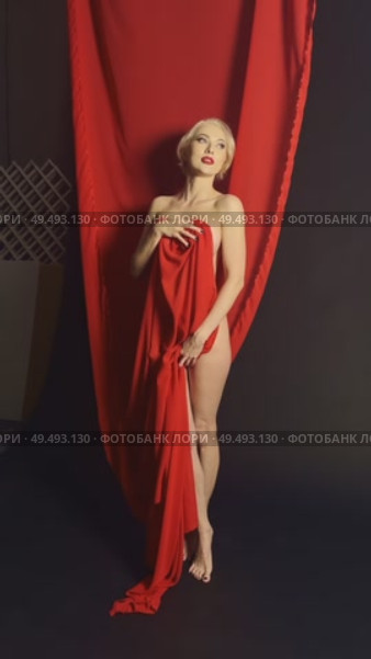 Model posing elegantly with red fabric in a dramatic indoor setup. Стоковое видео, видеограф Гурьянов Андрей / Фотобанк Лори