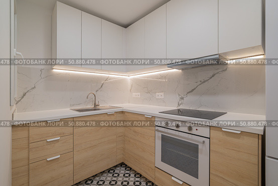 Modern kitchen with white cabinets and wooden accents. Features a marble backsplash, stainless steel appliances, and patterned floor tiles. Стоковое фото, фотограф PAv / Фотобанк Лори