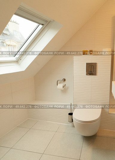 Modern white wc bowl in beige bathroom toilet, mansard roof and window. Moder luxury bathroom. Стоковое фото, агентство Ingram Publishing / Фотобанк Лори