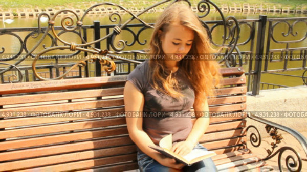 Молодая девушка читает книгу, сидя на скамейке. Лето, городской парк. Стоковое видео, видеограф Mikhail Erguine / Фотобанк Лори