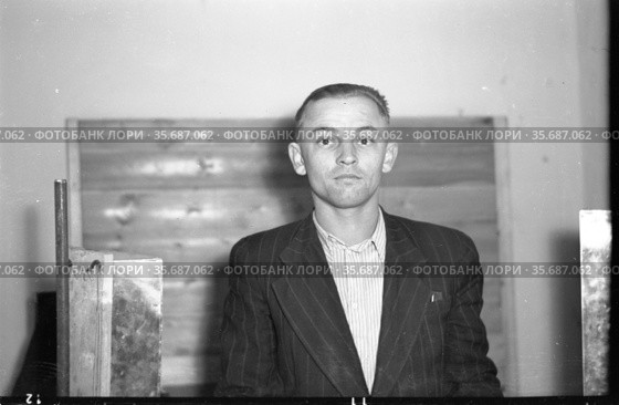 Молодой человек позирует, стоя в помещении, он смотрит в камеру с нейтральным выражением лица, мужчина одет в темный полосатый пиджак и светлую рубашку, город Киренск. Редакционное фото, фотограф Варфоломей Тетерин / Фотобанк Лори
