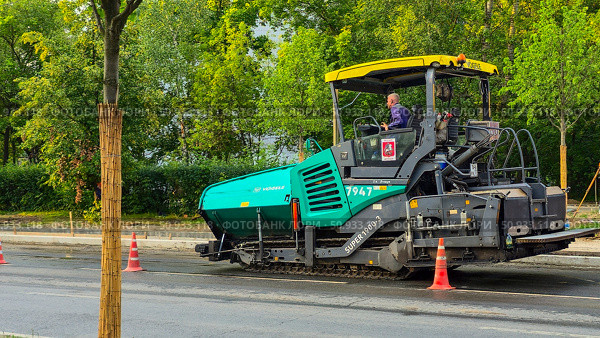 Moscow July 25 2025, Asphalt paver evenly distributes hot bituminous material on the road. Редакционное фото, фотограф Скрипачев Антон / Фотобанк Лори