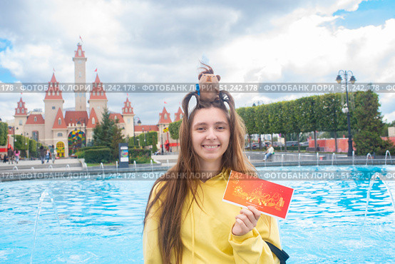 Москва, Россия. 4 сентября 2025 года. Девочка-подросток или молодая женщина с ободком с игрушечной капибарой на голове. Девушка держит билет в парк развлечений «Остров мечты» перед Замком, входом в парк.. Редакционное фото, фотограф Яна Проничева / Фотобанк Лори