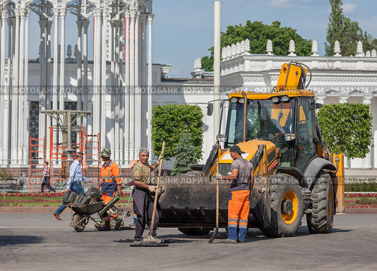 Москва, ВДНХ. Реконструкция 2017-2018 года. Рабочие - асфальтоукладчики стоят рядом с большим желтым трактором, оснащенным ковшом, на главной аллее. Редакционное фото, фотограф Наталья Николаева / Фотобанк Лори