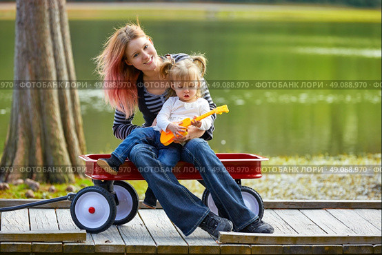 mother and daughter playing toy guitar in the park lake with pull cart. Стоковое фото, агентство Ingram Publishing / Фотобанк Лори