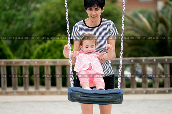 Mother swinging her little daughter on a swing in a playground. Стоковое фото, агентство Ingram Publishing / Фотобанк Лори