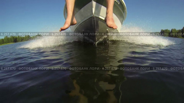 Моторная лодка едет по озеру, ноги свисают с носа катера. Вид снизу, спереди. Стоковое видео, видеограф Кекяляйнен Андрей / Фотобанк Лори