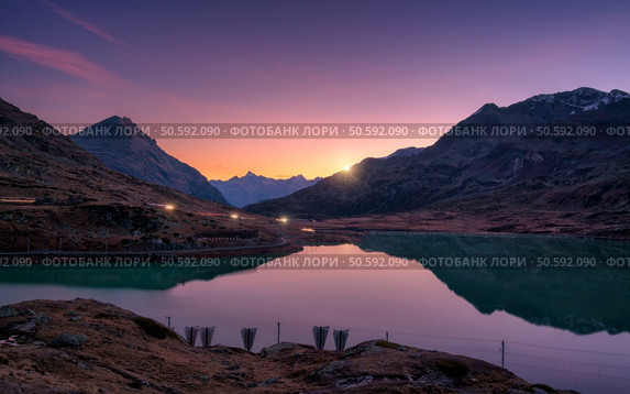 Mountain peaks mirrored in a tranquil alpine lake in autumn at sunset. Lake Bianco, Switzerland in fall. Colorful landscape with mountains, reflection in water, purple sky at dusk.  Swiss alps	. Стоковое фото, агентство Ingram Publishing / Фотобанк Лори