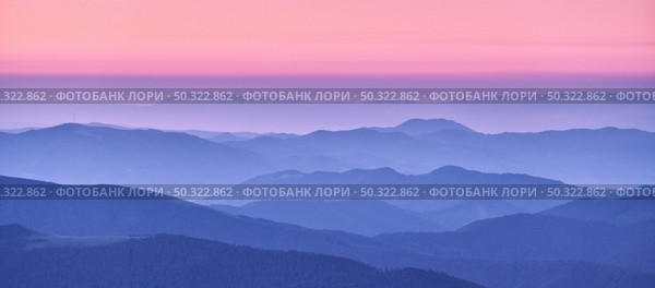 Mountain ridges in fog and pink sky at sunset in autumn. Beautiful landscape with foggy mountain valley, hills, forest at dusk in blue hour in fall. Aerial view of hills. Top view. Nature background. Стоковое фото, агентство Ingram Publishing / Фотобанк Лори