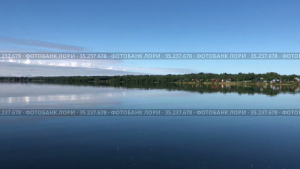 Moving on surface of large forest lake. Blue sky reflecting in calm water. Village is on shore in countryside. Karelia, Russia. Стоковое видео, видеограф Кекяляйнен Андрей / Фотобанк Лори