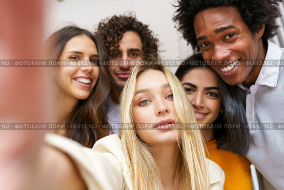 Multi-ethnic group of friends taking a selfie together while having fun in the street. Blonde Russian woman in the foreground.. Multi-ethnic group of friends taking a selfie together while having fun outdoors. Стоковое фото, агентство Ingram Publishing / Фотобанк Лори