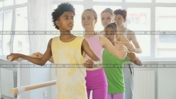 Multiethnic group of teenage girls and boys, ballet class students, practicing demi plie at barre during lesson for beginners under guidance of female teacher in light-filled choreography studio. Стоковое видео, видеограф Яков Филимонов / Фотобанк Лори