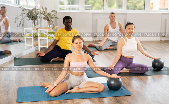 Multinational athletes sitting on floor in asana pigeon do body tilts to side, use fitball. Стоковое фото, фотограф Яков Филимонов / Фотобанк Лори