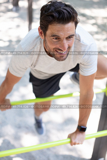 muscular build man doing pull ups exercises on horizontal bars. Стоковое фото, агентство Ingram Publishing / Фотобанк Лори