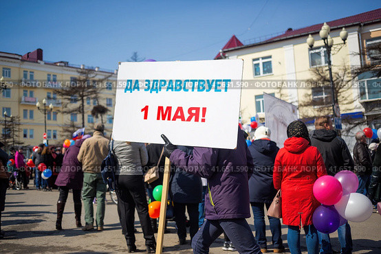 Мужчина несет плакат с надписью "Да здравствует 1 мая!". Первомайская демонстрация. Митинг и праздничное шествие по улице города. Магадан, Магаданская область, Россия. (2018 год). Редакционное фото, фотограф Андрей Степанов / Фотобанк Лори