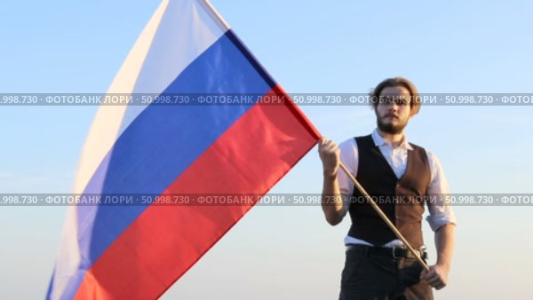 Мужчина с флагом России на фоне неба. Стоковое видео, видеограф 1Andrey Милкин / Фотобанк Лори
