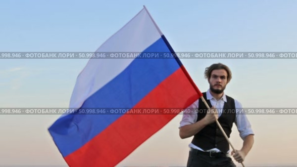 Мужчина с флагом России наперевес решительно идет в сторону камеры. Стоковое видео, видеограф 1Andrey Милкин / Фотобанк Лори