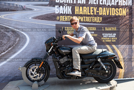 Мужчина в очках фотографируется на мотоцикле Harley-Davidson. Розыгрыш мотоцикла на фестивале Харли дэйз в Санкт-Петербурге (2018 год). Редакционное фото, фотограф Кекяляйнен Андрей / Фотобанк Лори