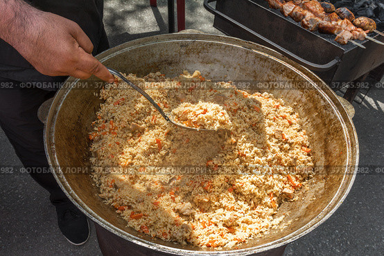 На уличном рынке продаются вкусный горячий плов и шашлык. Повар помешивает рис половником. Праздник сабантуй. Стоковое фото, фотограф Александр Бушков / Фотобанк Лори