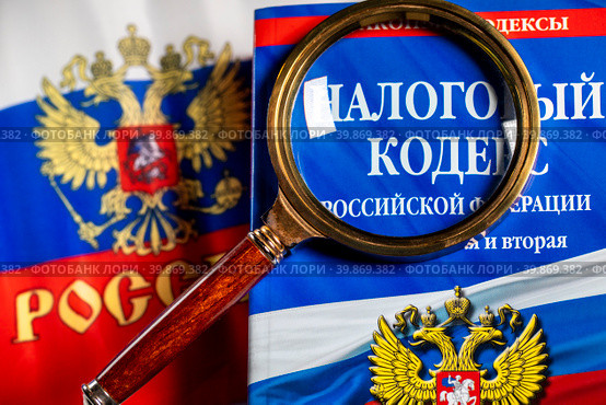 Налоговый кодекс под увеличительным стеклом лежат на столе (2023 год). Редакционное фото, фотограф Николай Винокуров / Фотобанк Лори