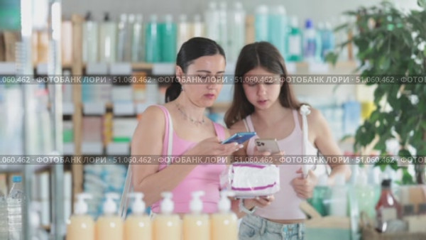 Near display case in pharmacy, woman with daughter scans barcode on female pads, reads user manual. Client studies product in detail, collects information online. Стоковое видео, видеограф Яков Филимонов / Фотобанк Лори
