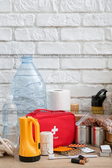 Necessities for emergency bag on wooden table near white brick wall. Стоковое фото, фотограф Pixel_shot / Фотобанк Лори