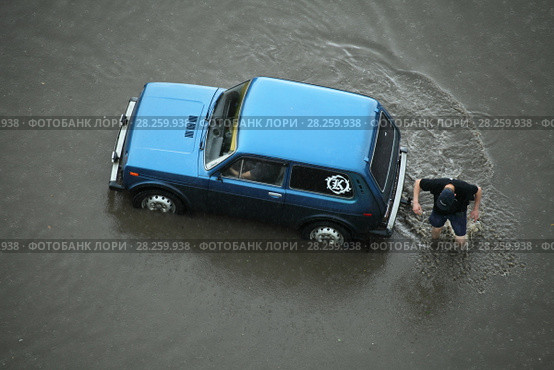 Незадачливый водитель и его пассажир оказались в водной ловушке на полностью затопленной улице. Город Петрозаводск (2016 год). Редакционное фото, фотограф Сергей Цепек / Фотобанк Лори