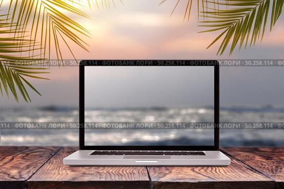 Notebook monitor with blurred seascape sunrise picture on a wooden table against the same background with green palm leaves frame, copy space. Working at sea, outside office concept.. Laptop screen with blurred sea background. Стоковое фото, агентство Ingram Publishing / Фотобанк Лори