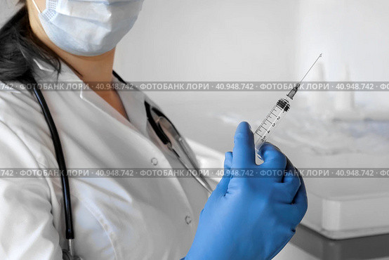 Nurse pushing air out of syringe for vaccine injection. Doctor wearing blue gloves and medical mask. Person holds a syringe with medicine in his hand Close Up. She ready to give an injection. Science. Стоковое фото, фотограф Марина Демидюк / Фотобанк Лори