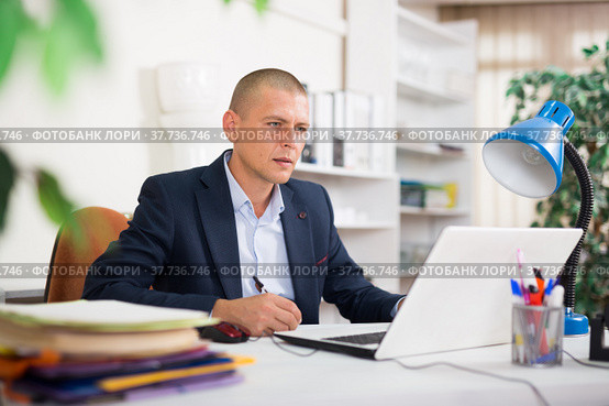 Office employee focused on working with laptop and papers. Стоковое фото, фотограф Яков Филимонов / Фотобанк Лори