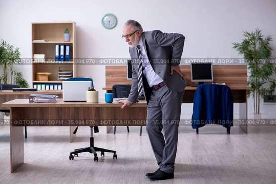 Old male employee suffering from radiculitis at workplace. Стоковое фото, фотограф Elnur / Фотобанк Лори