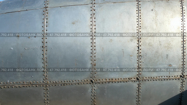 Old metal silver surface of the aircraft fuselage with rivets. Стоковое AI-изображение, AI-художник Sergey Grishin / Фотобанк Лори