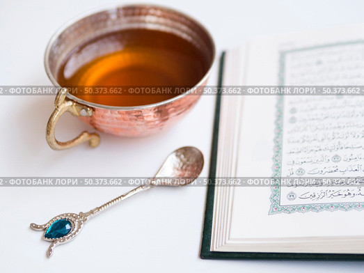 OLYMPUS DIGITAL CAMERA. close up opened quran with tea cup. Редакционное фото, агентство Ingram Publishing / Фотобанк Лори
