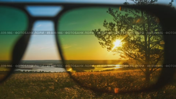 On a summer day, a man put on sunglasses to protect his eyes from the sun and admired the rising sun over the hills and fields. Close up. Стоковое видео, видеограф Strunov David / Фотобанк Лори