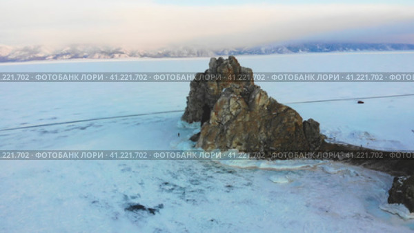 Overflight of Shamanka Rock or Cape Burkhan in winter. Frozen Lake Baikal, covered with snow. Ice road at the famous rock. Облет скалы Шаманка или мыса Бурхан зимой. Замерзшее озеро Байкал, покрытое снегом. Стоковое видео, видеограф Виктория Тельминова / Фотобанк Лори