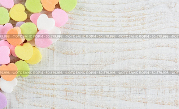 Overhead shot of a group of pastel candy Valentine’s hearts in the upper right corner and side of the frame. Horizontal format on a whitewashed rustic wooden table with copy space. Стоковое фото, агентство Ingram Publishing / Фотобанк Лори