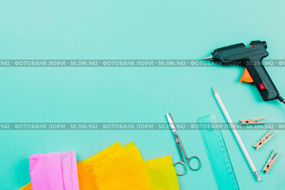 overhead view yellow pink paper scissor ruler pencil clothespins electric glue gun turquoise background. Стоковое фото, агентство Ingram Publishing / Фотобанк Лори