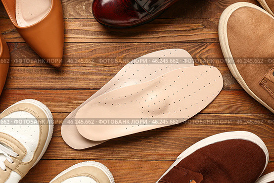 Pair of leather orthopedic insoles and different shoes on wooden background, closeup. Стоковое фото, фотограф Pixel_shot / Фотобанк Лори