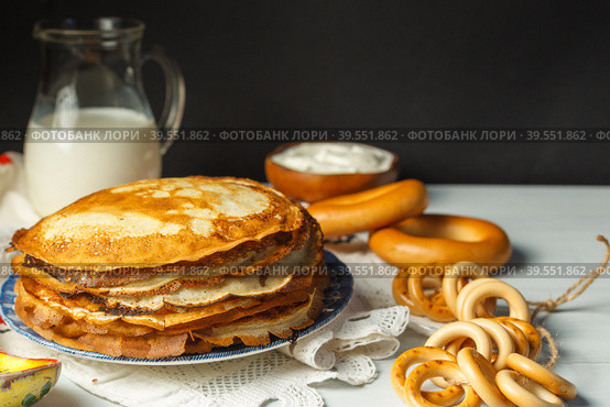 Pancakes in a stack, on a wooden table, with sour cream, a jug of milk and bagels. Close-up, selective focus. Стоковое фото, фотограф Bogdanova Mariia / Фотобанк Лори