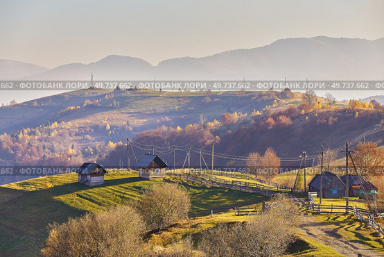 Panoramic view of misty sunny autumn evening in mountains. Beautiful sunset hills landscape. Slopes, meadows, fields, village, house, dirt road. Amazing fall rural scene. Carpathian range. Ukraine. Стоковое фото, агентство Ingram Publishing / Фотобанк Лори