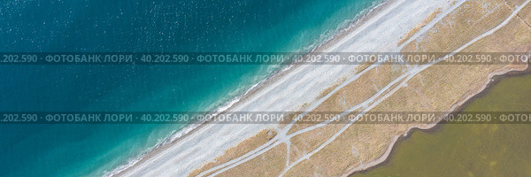 Панорамный вид сверху на галечную косу, разделяющую море и соленое озеро. Чистая бирюзовая морская вода и желто-зеленая вода в мелком озере. На косе грунтовые дороги. Стоковое фото, фотограф Андрей Степанов / Фотобанк Лори
