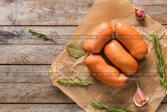 Parchment with tasty sausages on wooden table. Стоковое фото, фотограф Pixel_shot / Фотобанк Лори