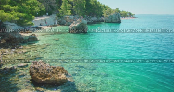 People enjoy turquoise waters and rocky coastline of Makarska cove in Croatia. Стоковое видео, видеограф Igor Tichonow / Фотобанк Лори